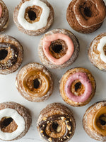 Load image into Gallery viewer, Set of assorted cronut dessert pastry topped with dulce de leche, tiramisu, vanilla, strawberry, hazelnut, and mixed berry icing. 
